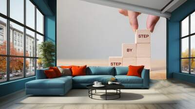 Hand arranging wood block stacking as step stair on top with word Step By Step. Business concept for personal ladder of success process Wall mural