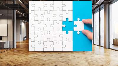 Hand putting piece of white jigsaw puzzle on blue background. Team business success partnership or teamwork. Wall mural