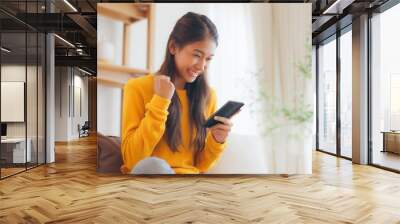 Happy young asian woman relax on comfortable couch at home texting messaging on smartphone, smiling girl use cellphone, chatting online message, shopping online from home Wall mural