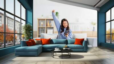 Happy young asian woman relax on comfortable couch at home texting messaging on smartphone, smiling girl use cellphone, chatting online message, shopping online from home Wall mural