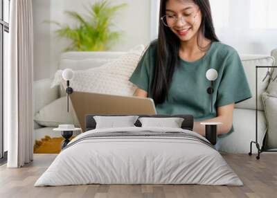 Smiling young asian woman working on laptop at home. Attractive asia female using computer remote studying, watching online education and video calling Wall mural