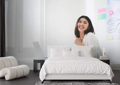 Successful business woman working in a workplace. She feels happy and smiles. Computer laptop and paperwork on desk Wall mural