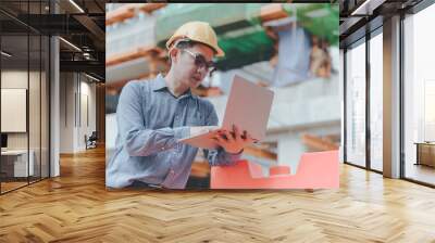 Young asian engineers are working on the construction site. Wear a yellow helmet safety. Hand holding computer laptop Wall mural