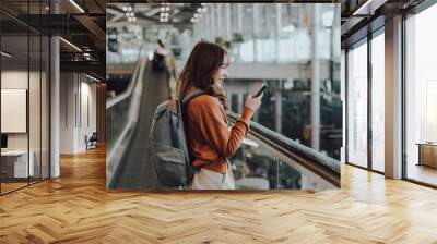 Young asian woman in international airport terminal or modern train station. Backpacker passenger female commuter walking on escalator Wall mural