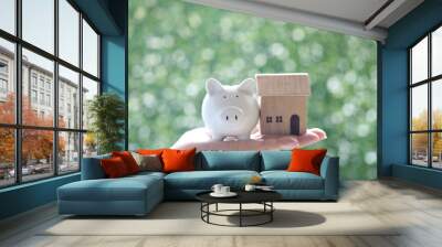 Selective focus of Woman hand holding piggy with model house on natural green background, Business investment and real estate concept Wall mural