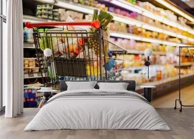 A shopping cart with grocery products in a supermarket Wall mural