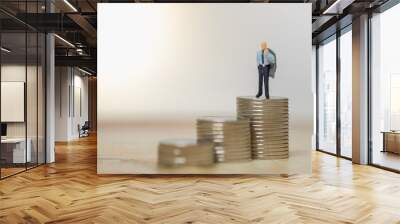 Money and Business Concept. Businessman holding grey jacket on shoulder miniature figure standing on top of stack of coins. Wall mural