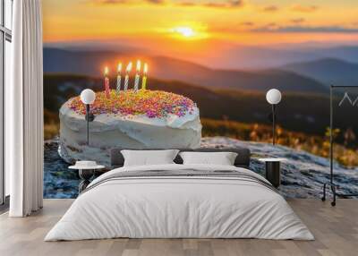 A birthday cake adorned with sprinkles and candles sits on a rock at sunset Wall mural