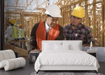 Architect and foreman having discussion over blueprint with workers in background at construction site Wall mural