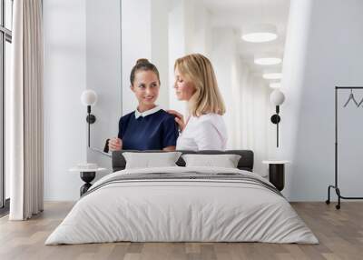 Businesswomen discussing over document while standing in corridor at office Wall mural