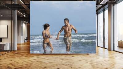 Cheerful semidressed couple running in surf at beach Wall mural