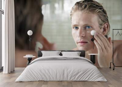 Closeup of handsome young man applying facial cream in front of mirror Wall mural