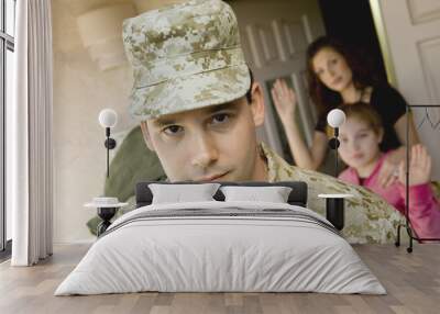 confident military man leaving house with family waving in background Wall mural