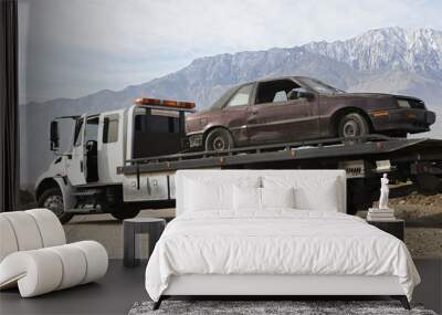 damaged car being transported on tow truck with mountain range in the background Wall mural