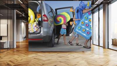 Father and two children unloading beach accessories from car Wall mural