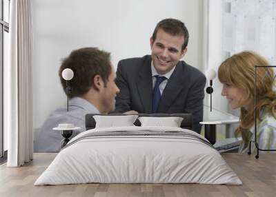 Friendly male real estate agent handing house key to a smiling young couple in office Wall mural