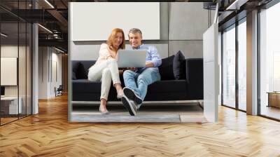 Full-length of smiling couple using laptop on sofa Wall mural