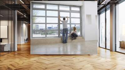 Full length rear view of a couple looking out of window in empty apartment Wall mural