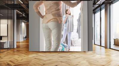 Full-length rear view of mother watching daughters trying on clothes in room Wall mural