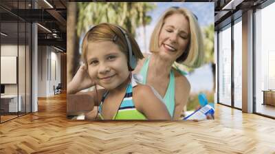 Grandmother applying sunscreen to girl (7-9) listening to headphones portrait. Wall mural