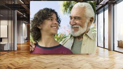 Happy mixed race boy looking at his senior grandfather outdoors Wall mural