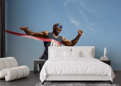 Low angle view of an African American male runner winning race against blue sky Wall mural