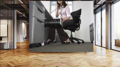 Low section of young businesswoman talking on telephone while opening drawer in office Wall mural