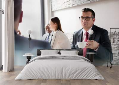 Mature businessman having coffee while talking with male colleague in office cafeteria Wall mural