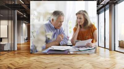 Mature couple with bills sitting at dining table in house Wall mural