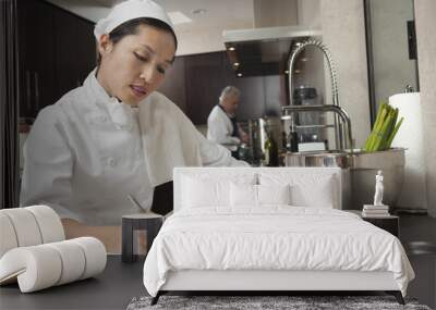 Middle aged female chef writing on clipboard with colleague working in background Wall mural