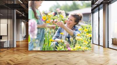 Mother and daughter picking pretty colourful flowers in their organic garden Wall mural