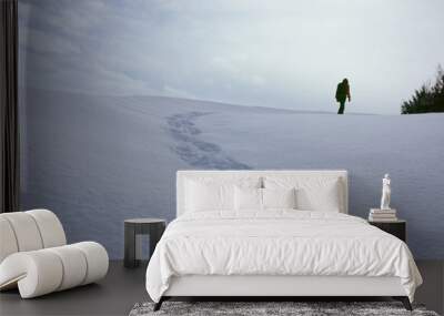 Person walking on snow covered land leaving behind trail of footprints Wall mural