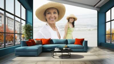 Portrait of happy woman with young daughter walking at beach Wall mural