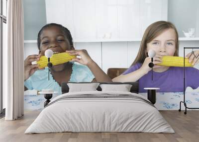 Portrait of two multiethnic girls eating corn cobs at table Wall mural