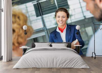 Portrait of young attractive passenger service agent giving boarding with passenger after check in at airport Wall mural