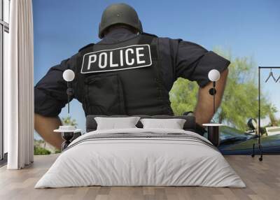 Rear view of policeman in uniform standing against car Wall mural