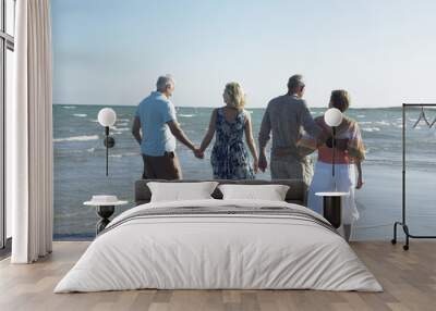 Rear view of two couples walking together on tropical beach Wall mural