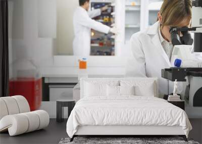 scientist using microscope with male colleague looking in refrigerator in laboratory Wall mural