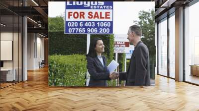 side view of a female real estate agent shaking hands with middle aged man by for sale signs Wall mural