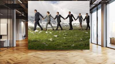 Side view of business people holding hands and walking through mountains Wall mural