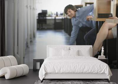 Smiling businessman picking pen off floor near woman's legs in office Wall mural