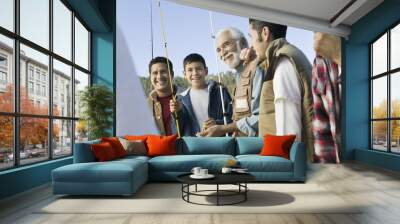 Smiling male members of three generation family holding fishing rods outdoors Wall mural