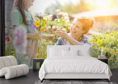 Smiling mother giving flowers to daughter while gardening at farm Wall mural