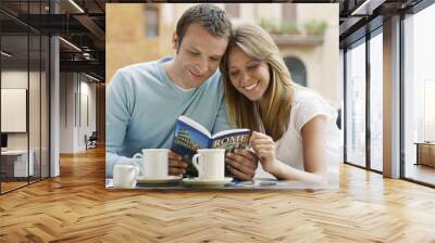 Smiling young couple at outdoor cafe looking at guidebook of Rome Wall mural