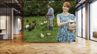 Young smiling couple feeding hens on grassland Wall mural