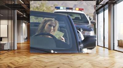 Young woman in car reading ticket with traffic cop in the background Wall mural