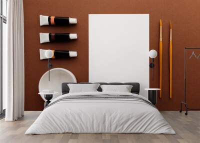 A blank white paper with two different size brush, a white bowl and paints on brown background. Flat lay top view image for creative painting projects.  Wall mural