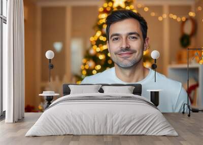 A handsome young man in a white t-shirt on the background of a Christmas tree, a Portrait of a handsome man in a room decorated for Christmas. Man looking at the camera Wall mural