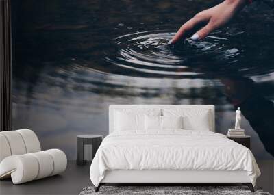 Girl touches the surface of the water on the lake with her fingers Wall mural