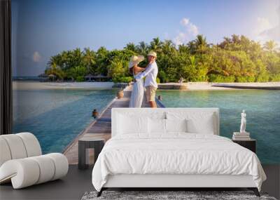 A beautiful couple stands hugging on a wooden pier over turquoise sea in the Maldives islands during their romantic holiday time Wall mural